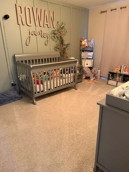 A completed nursery cleaning project featuring an organized crib and vacuumed carpet under a personalized wall sign.