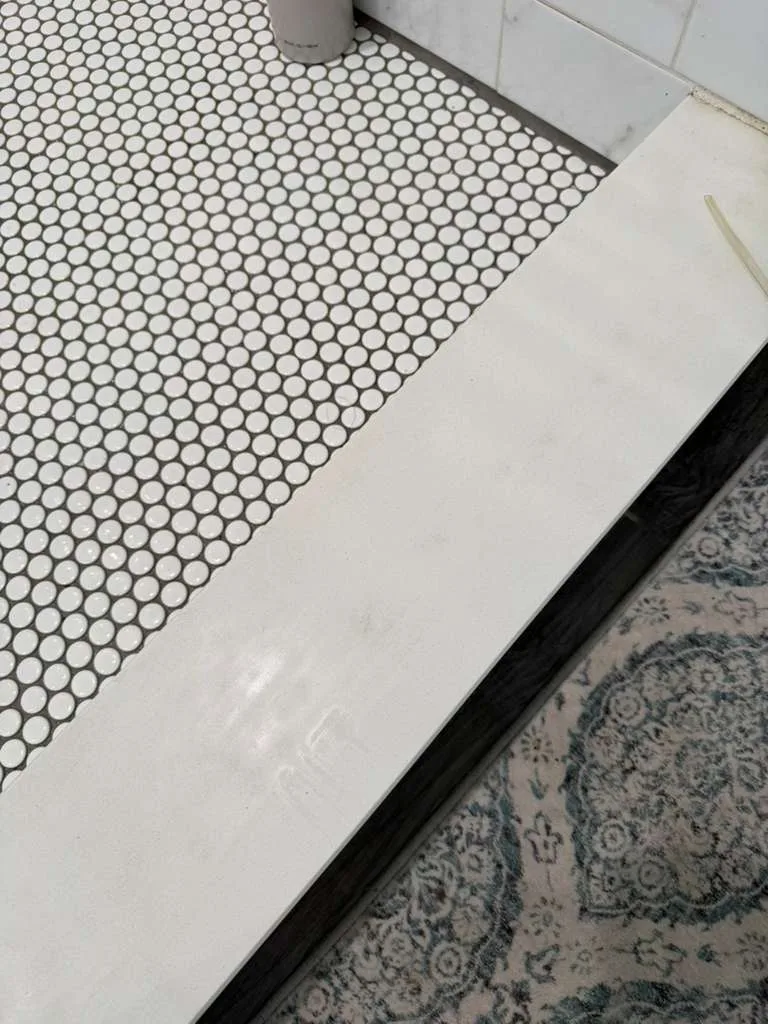 A pristine white stone threshold next to tiled flooring, displaying the clear results completed after the shower curb cleaning.