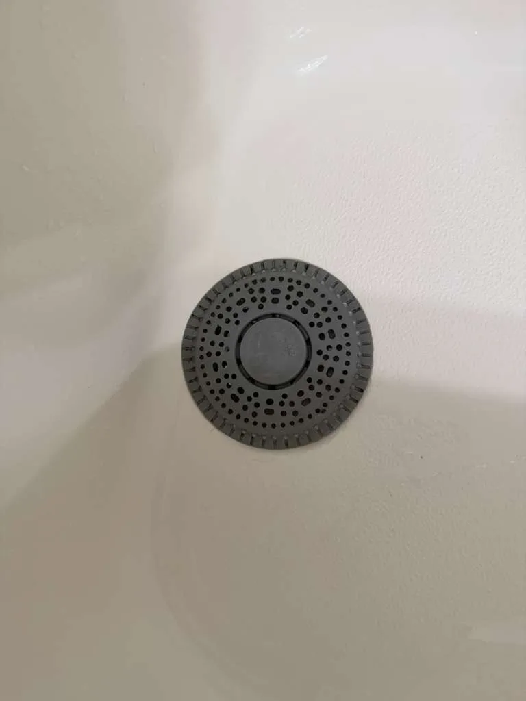 A grey silicone hair catcher over a tub after a successful shower drain cleaning