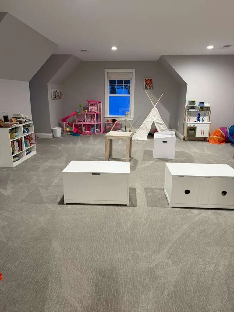 The completed playroom organization and cleaning project, showing a tidy room with organized toys and visible vacuum lines on the carpet.