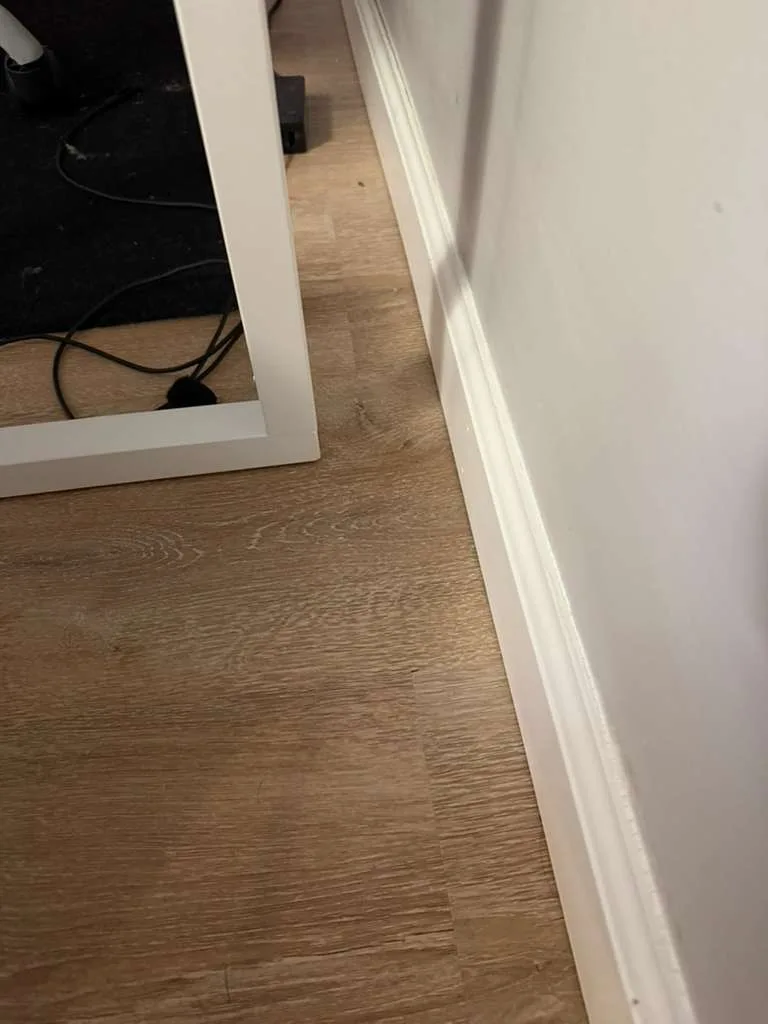 The final result of a professional baseboard and corner cleaning showing a spotless floor and sanitized white trim.